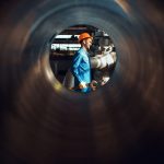 Worker with wrench on factory, view through tube